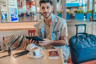 Cheerful Mansitting In Coffee Shop At Airport Station While Sitting Near Luggage