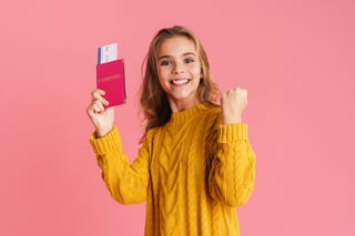 Glückliches Mädchen mit Siegergeste und Reisepass mit Tickets isoliert auf rosa Hintergrund
