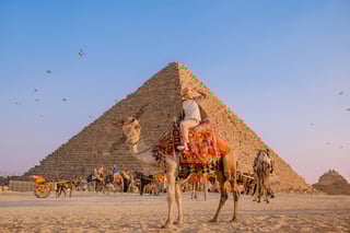 Happy Tourist Man With Hat Riding On Camel Background Pyramid Of Egyptian Giza Sun Light